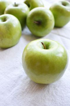 several green apples sitting on top of a white table cloth next to eachother