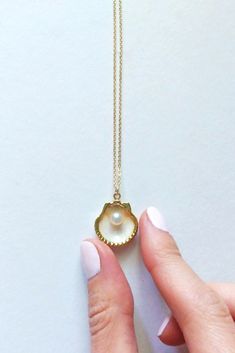 a woman's hand holding a necklace with a pearl in the middle and a shell on it