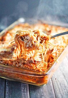 a glass casserole dish filled with pasta and meat being spooned into it