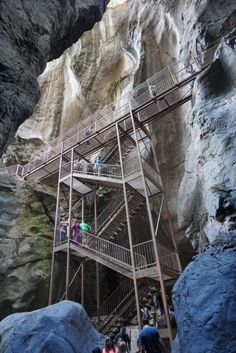 several people are walking up and down the stairs in a cave with large rocks on either side