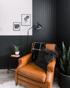 a brown leather chair sitting next to a black and white wall with pictures on it