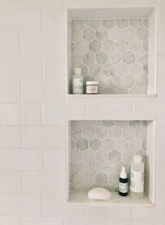 two white shelves with bottles and soaps on them in a tiled shower stall area