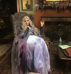 a barbie doll sitting on a chair in a living room with a fire place and fireplace