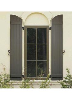 an open window with shutters on the side of a building and plants in front of it