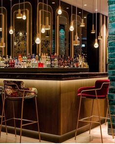 two bar stools are in front of the bar with bottles on it and lights hanging from the ceiling