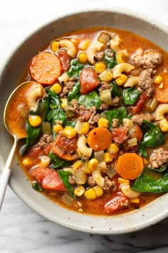 a white bowl filled with meat, vegetables and pasta soup on top of a marble counter