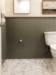 a white toilet sitting in a bathroom next to a wooden paneled wall with pictures above it