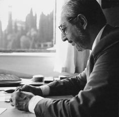 a man sitting at a desk in front of a laptop computer and writing on a piece of paper