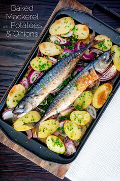 baked mackerel with potatoes and onions in a baking pan on a wooden table