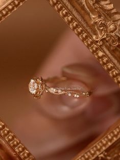 a close up of a diamond ring in a gold frame with the reflection of someone's hand