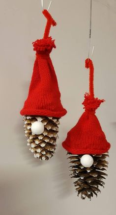 two pine cones are hanging from the ceiling with red knitted hats on them, and one has white balls attached to it