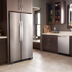 a stainless steel refrigerator in a kitchen with brown cabinets and tile flooring, along with white counter tops