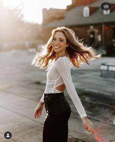 a woman is walking down the street with her hair blowing in the wind and smiling