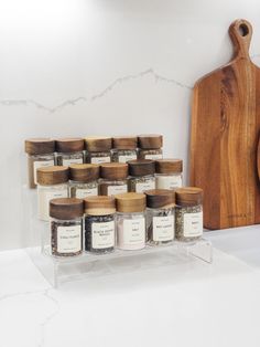 spice jars are stacked on a clear shelf next to a cutting board and wooden spoon