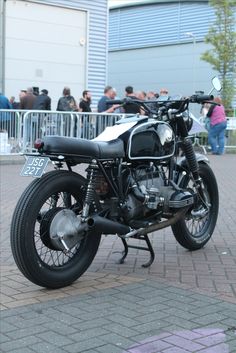 a black motorcycle parked on top of a brick road next to a crowd of people