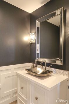 a bathroom sink sitting under a mirror next to a wall mounted light above it's vanity