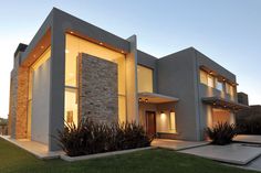 a modern house is lit up at night with lights on the windows and plants in front