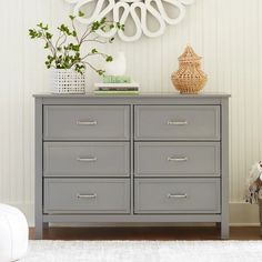 a grey dresser with two drawers and a clock on the wall above it in a white room