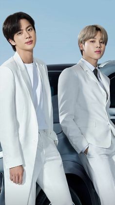 two young men in white suits standing next to each other near a black and white car