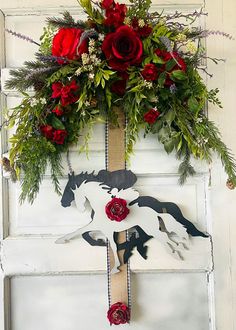 a white door decorated with red roses and greenery next to a wooden horse decoration