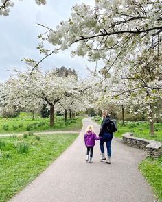 a mother and daughter walking down a path in the park with cherry blossoms on trees