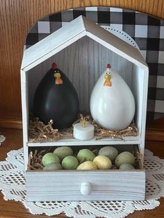 two white vases sitting on top of a wooden shelf filled with eggs and grass