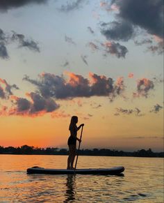 a woman is standing on a paddle board in the water as the sun goes down