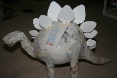 a paper mache dinosaur with white wings on it's back