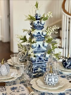 a blue and white table setting with flowers in vases on the centerpiece, china dishes to the side