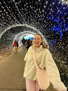 a woman walking down a walkway covered in christmas lights and holding onto a pink handbag