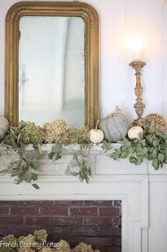 a mantel with pumpkins and greenery on it, next to a mirror