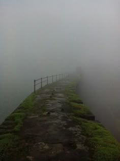 a long stone wall with grass growing on it and fog in the sky behind it