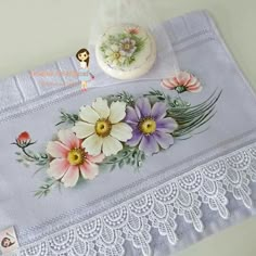 an embroidered table runner with flowers on it and a doll next to the lace edge