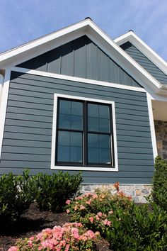 a blue house with white trim and windows on the side, surrounded by plants and flowers