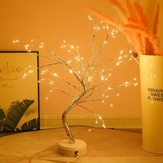 there is a small tree with lights in the vase on the table next to it