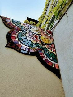 an artistic stained glass piece on the side of a building with flowers growing out of it