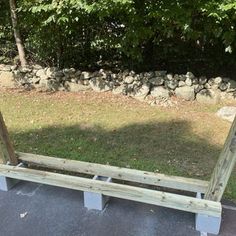 a wooden bench sitting in the middle of a park next to a stone wall and trees