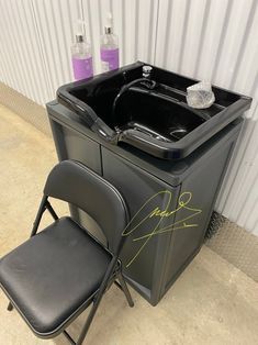 a black chair sitting in front of a portable bathtub with the seat up next to it