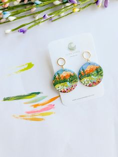 a pair of earrings sitting on top of a white table next to some colorful flowers