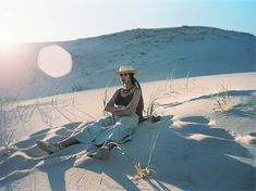 a man sitting on top of a sandy beach next to tall grass and a white frisbee