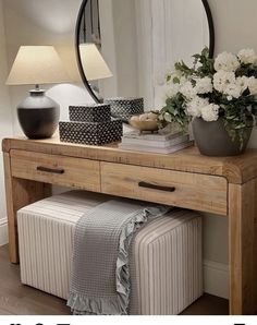 a wooden table topped with a mirror next to a lamp and vase filled with flowers