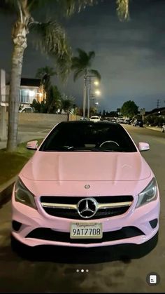 a pink car is parked on the side of the road at night with palm trees in the background