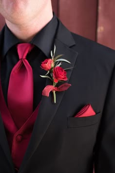 a man wearing a black suit with red flowers on it's lapel flower