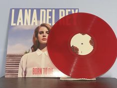 a red vinyl record sitting on top of a wooden table next to a magazine cover