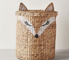 a woven basket with a fox face painted on the front and sides, sitting on a table