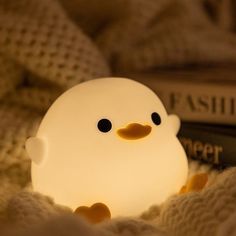 a small light that looks like a ducky sitting on a bed next to a book