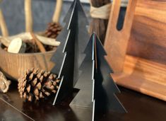 a wooden bowl filled with pine cones next to a metal christmas tree on top of a table