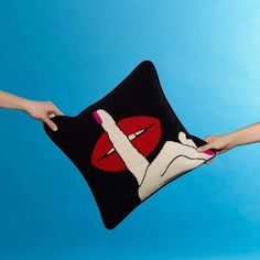 two hands holding a black pillow with red lips on it against a blue sky background