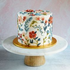 a decorated cake sitting on top of a white plate next to a wooden stand and pink wall