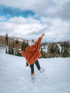 a person jumping in the air on a snow covered slope with trees and mountains in the background